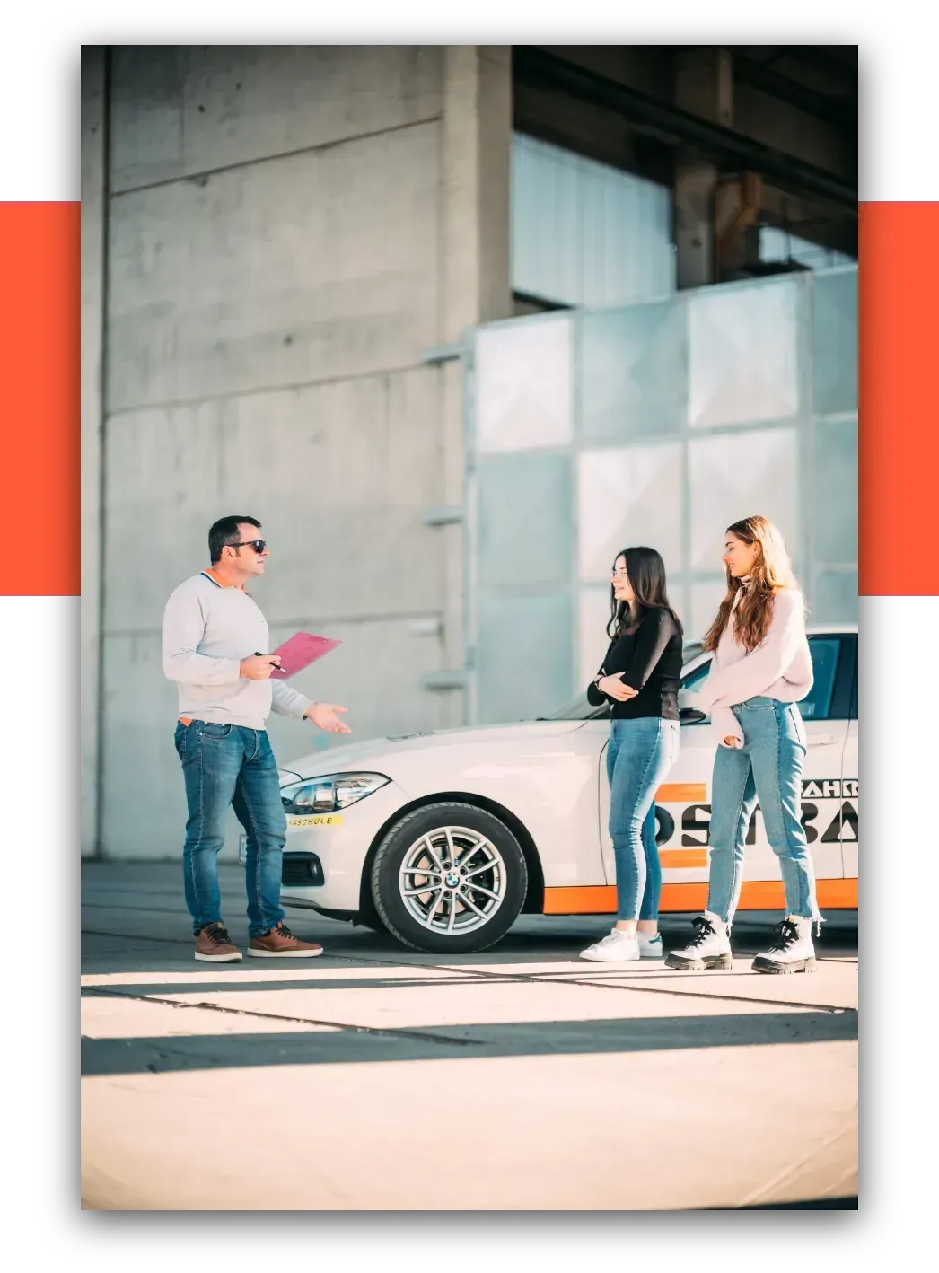 Ein Fahrlehrer bespricht mit zwei Fahrschülerinnen die Fahrstunde neben dem Fahrschulauto