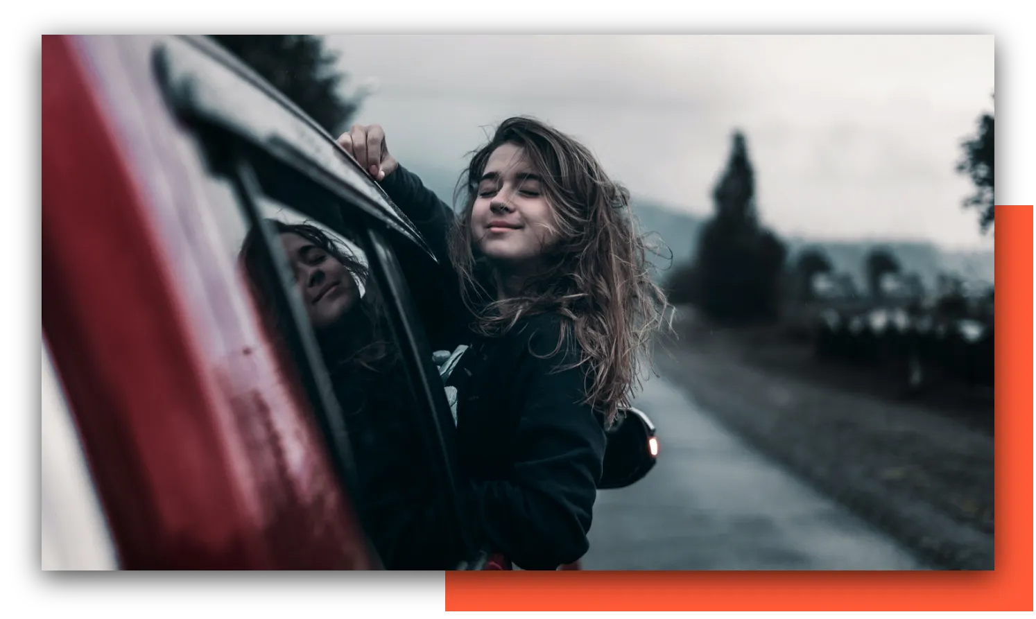 Eine junge Frau lehnt sich lachend aus dem Fenster eines fahrenden Autos